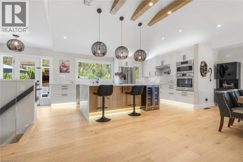 Modern kitchen featuring wood-finish flooring, white cabinetry, a center island with seating, integrated appliances, and exposed ceiling beams - 293 North Shore Boulevard E, Burlington, ON 
