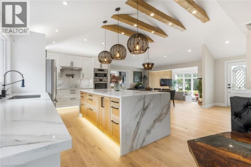 Kitchen featuring a large island with waterfall countertop, pendant lighting, built-in appliances, and wood-finish flooring - 293 North Shore Boulevard E, Burlington, ON 