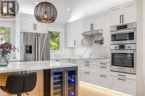 White shaker cabinetry with black hardware, stainless steel appliances, marble-patterned backsplash, light wood-finish flooring, and under-cabinet lighting - 293 North Shore Boulevard E, Burlington, ON 