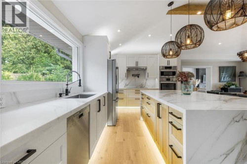 Spacious kitchen featuring white cabinetry, integrated stainless steel appliances, a large center island with a stone countertop, and wood-finish flooring - 293 North Shore Boulevard E, Burlington, ON 