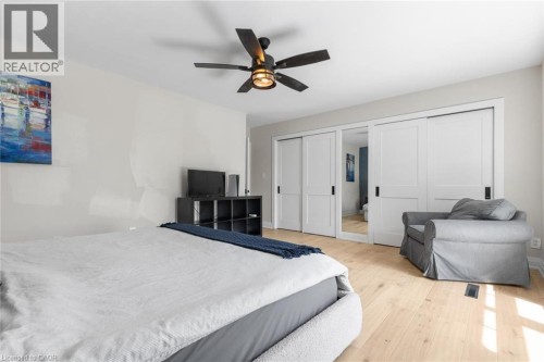 Light wood-finish flooring, ceiling fan with integrated lighting, and multiple sliding closet doors with black hardware - 293 North Shore Boulevard E, Burlington, ON 