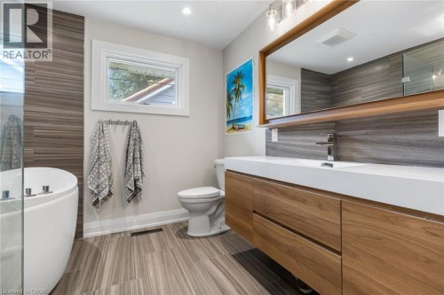 Contemporary bathroom featuring a floating wood-finish vanity with an integrated white sink, a freestanding soaking tub, wood-finish wall paneling, and wood-finish flooring - 293 North Shore Boulevard E, Burlington, ON 
