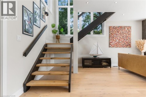 Modern open-concept living space featuring a striking floating staircase with dark metal railings and wood-finish treads, light wood flooring throughout, and abundant natural light from large multi-pa - 293 North Shore Boulevard E, Burlington, ON 
