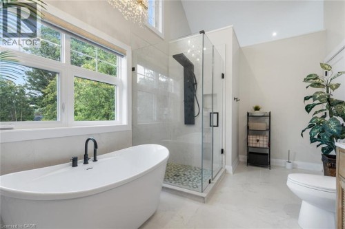 Freestanding soaking tub with matte black fixtures, glass-enclosed shower with a black panel shower system, vaulted ceiling, and white tile flooring - 293 North Shore Boulevard E, Burlington, ON 
