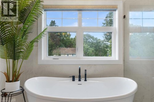 Freestanding soaking tub with matte black fixtures, set against a window with white trim, and light-toned tile wall covering - 293 North Shore Boulevard E, Burlington, ON 