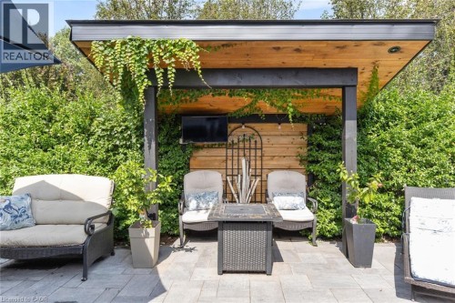 Paved patio area featuring a wooden pergola with integrated lighting, a slatted wood accent wall, and established perimeter hedges - 293 North Shore Boulevard E, Burlington, ON 