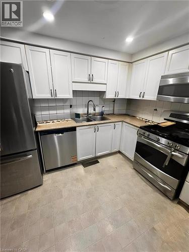 Kitchen featuring white shaker-style cabinetry, stainless steel appliances, a double basin sink with a high-arc faucet, and tiled flooring - 717 Activa Avenue, Kitchener, ON 