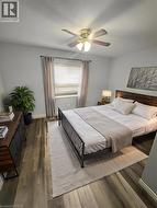 Window with blinds and drapes, wood-finish flooring, ceiling fan with light fixture, and a built-in wood-finish headboard - 