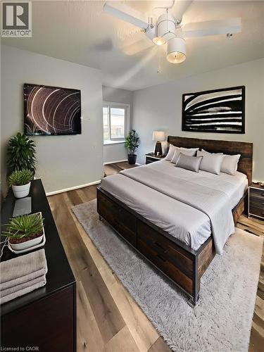Master bedroom featuring a wood-finish bed frame, neutral bedding, wood-finish flooring throughout, and a ceiling fan with integrated lighting - 717 Activa Avenue, Kitchener, ON 