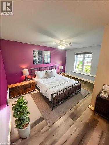 Primary Bedroom featuring a striking magenta accent wall, wood-finish flooring throughout, a black metal bed frame, dual bedside tables with integrated lighting, a large multi-pane window with natural - 717 Activa Avenue, Kitchener, ON 