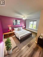 Primary Bedroom featuring a striking magenta accent wall, wood-finish flooring throughout, a black metal bed frame, dual bedside tables with integrated lighting, a large multi-pane window with natural - 