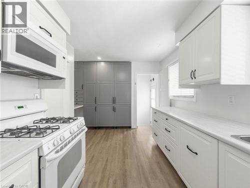 White cabinetry, white countertops, built-in microwave, gas range, and wood-finish flooring - 220 Cairn Street, London, ON 