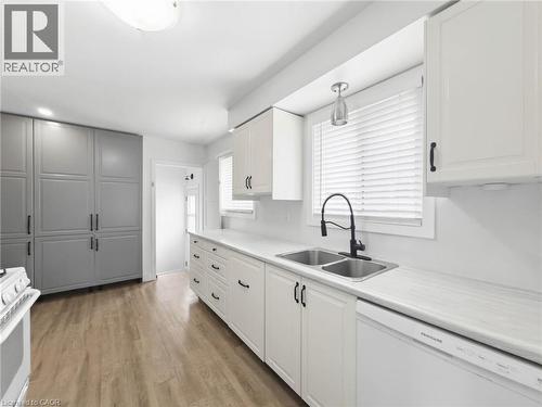 Dual-tone cabinetry, white countertops, wood-finish flooring, and a stainless steel double basin sink with a matte black faucet - 220 Cairn Street, London, ON 
