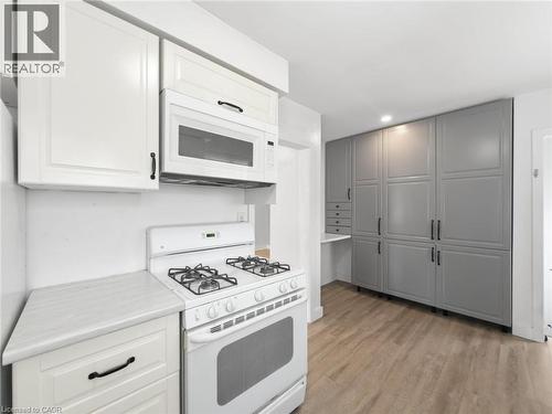 White cabinetry with dark pulls, over-the-range microwave, wood-finish flooring, and extensive built-in gray storage units - 220 Cairn Street, London, ON 