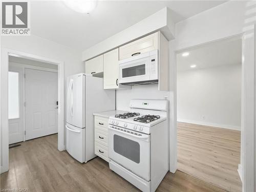 Kitchen featuring white appliances, upper and lower cabinetry, and wood-finish flooring - 220 Cairn Street, London, ON 