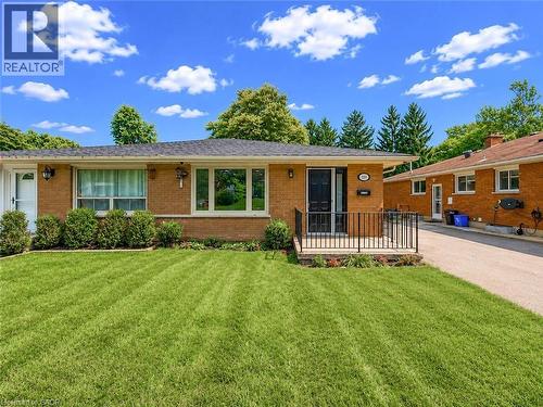 Brick exterior with a dark roof, featuring a covered entryway with a black door and wrought iron railing, a manicured lawn, and an asphalt driveway - 220 Cairn Street, London, ON 