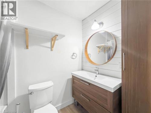 Bathroom with a wood-finish vanity, integrated sink, and an accent round mirror - 220 Cairn Street, London, ON 