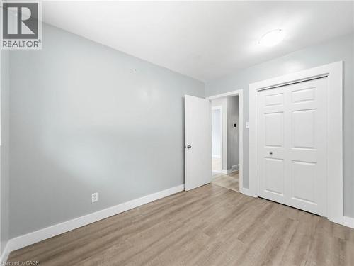 Light wood-finish flooring, light gray wall paint, overhead flush-mount lighting, white bi-fold closet doors, and white interior door - 220 Cairn Street, London, ON 