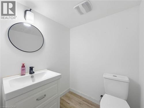 White vanity with integrated sink, black matte faucet, round mirror with black frame, and wood-finish flooring - 220 Cairn Street, London, ON 