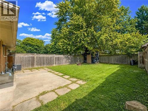 Expansive backyard featuring a concrete patio, stepping stone pathway, wood panel fencing, and mature trees - 220 Cairn Street, London, ON 