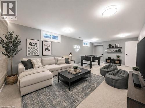 Carpeted recreational room featuring built-in floating shelves, flush-mount lighting, and egress windows - 220 Cairn Street, London, ON 