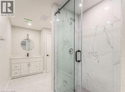 Spacious bathroom featuring a glass-enclosed shower with tile surround, white vanity with stone countertop, round wall-mounted mirror, and tile flooring - 
