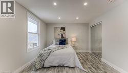 Recessed lighting illuminates the room, featuring wood-finish flooring and a window with white trim - 