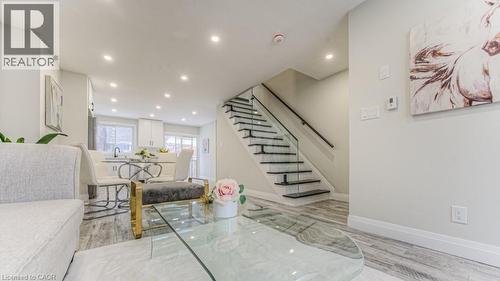 Recessed lighting, wood-finish flooring, glass panel staircase, black handrail, and white kitchen cabinetry - 152 Overlea Drive, Kitchener, ON 