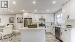 Kitchen featuring white cabinetry with black hardware, stainless steel appliances, a center island with a light-toned countertop, and wood-finish flooring - 