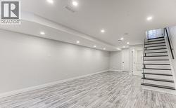 Recessed lighting, wood-finish flooring, white walls, black stair railing, and a white interior door - 