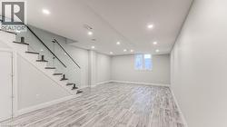 Finished lower level featuring recessed lighting, wood-finish flooring, a contemporary staircase with glass railing, and a window - 