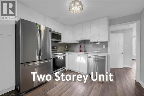 White cabinetry with stainless steel appliances, a gray subway tile backsplash, and wood-finish flooring - 9 Melrose Avenue S Unit# Upper, Hamilton, ON 