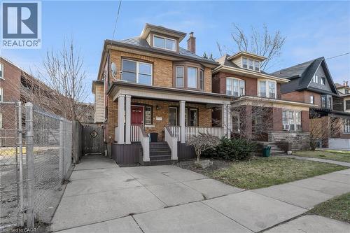 Brick exterior with multiple dormer windows, covered front porch, concrete driveway, and established front landscaping - 9 Melrose Avenue S Unit# Upper, Hamilton, ON 