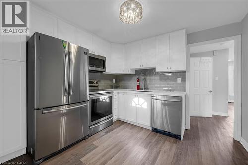 Kitchen featuring stainless steel appliances, white cabinetry, a subway tile backsplash, and wood-finish flooring - 9 Melrose Avenue S Unit# Upper, Hamilton, ON 