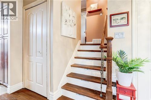 Wood-finish flooring with a white paneled door, staircase with wood treads, painted risers, and a wrought iron baluster - 106 Appleford Road, Hamilton, ON 