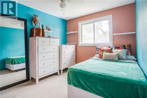 Bright bedroom featuring vibrant turquoise and coral accent walls, white wood cabinetry with multiple drawers for storage, large dual-pane window with natural light, carpeted flooring, and coordinated - 106 Appleford Road, Hamilton, ON 