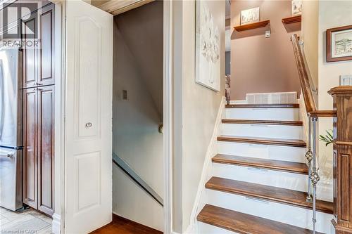 Staircase featuring wood-finish treads, white risers, and a decorative metal and wood-finish handrail - 106 Appleford Road, Hamilton, ON 