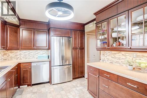 Cherry-toned cabinetry with crown molding, stainless steel appliances, mosaic tile backsplash, and light-toned countertops - 106 Appleford Road, Hamilton, ON 