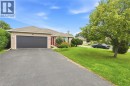 Brick exterior, attached garage with dark door, paved driveway, mature landscaping, and an expansive lawn - 9 Country Club Road, Cayuga, ON 
