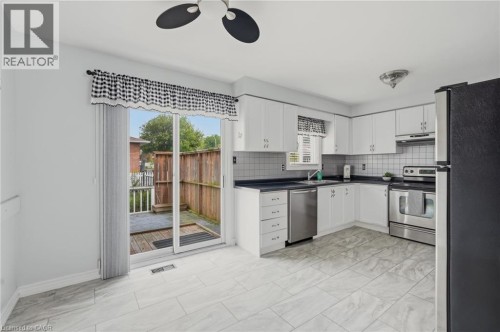 Kitchen featuring white cabinetry, stainless steel appliances, dark countertops, white tile backsplash, and light-toned tile flooring - 9 Country Club Road, Cayuga, ON 