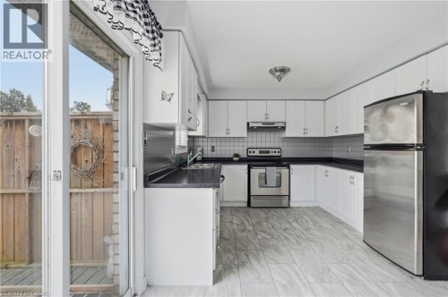 Kitchen featuring white cabinetry, dark countertops, tile flooring, stainless steel appliances, and a sliding glass door - 9 Country Club Road, Cayuga, ON 