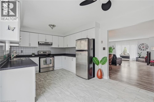 Kitchen featuring white cabinetry, dark countertops, a tile backsplash, stainless steel appliances, and tile flooring - 9 Country Club Road, Cayuga, ON 