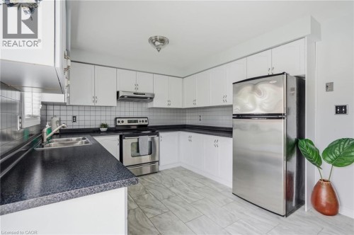 Kitchen featuring white cabinetry, dark countertops, stainless steel appliances, a tiled backsplash, and light-toned flooring - 9 Country Club Road, Cayuga, ON 