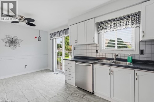 White cabinetry with dark countertops, stainless steel dishwasher, tile flooring, and a sliding glass door - 9 Country Club Road, Cayuga, ON 