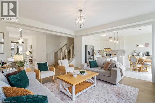 Open-concept living area with light wood-finish flooring, a contemporary chandelier, and a staircase with wood railing - 68 Barkerville Drive, Whitby, ON 