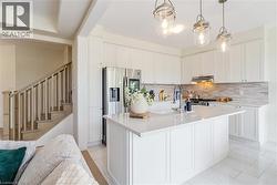 Kitchen featuring white cabinetry, a central island with an integrated sink, stainless steel appliances, and pendant lighting - 