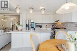 White cabinetry, stainless steel appliances, pendant lighting, light-toned countertops, and a tile backsplash - 