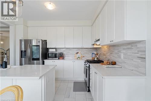White cabinetry, light countertops, mosaic tile backsplash, stainless steel appliances, and tile flooring - 68 Barkerville Drive, Whitby, ON 