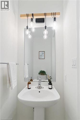 Pedestal sink with chrome faucet, wall-mounted mirror, and decorative light fixture with exposed bulbs - 68 Barkerville Drive, Whitby, ON 