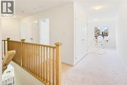Upper-level landing with light wood railing, neutral carpeting, and white walls - 